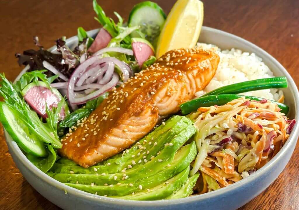 Village Crown Miso Salmon Bowl Dish containing Grilled Salmon, Chilli Slaw, Red Miso, Sushi Rice, Onion, Avocado, Radish, and Green Beans.
